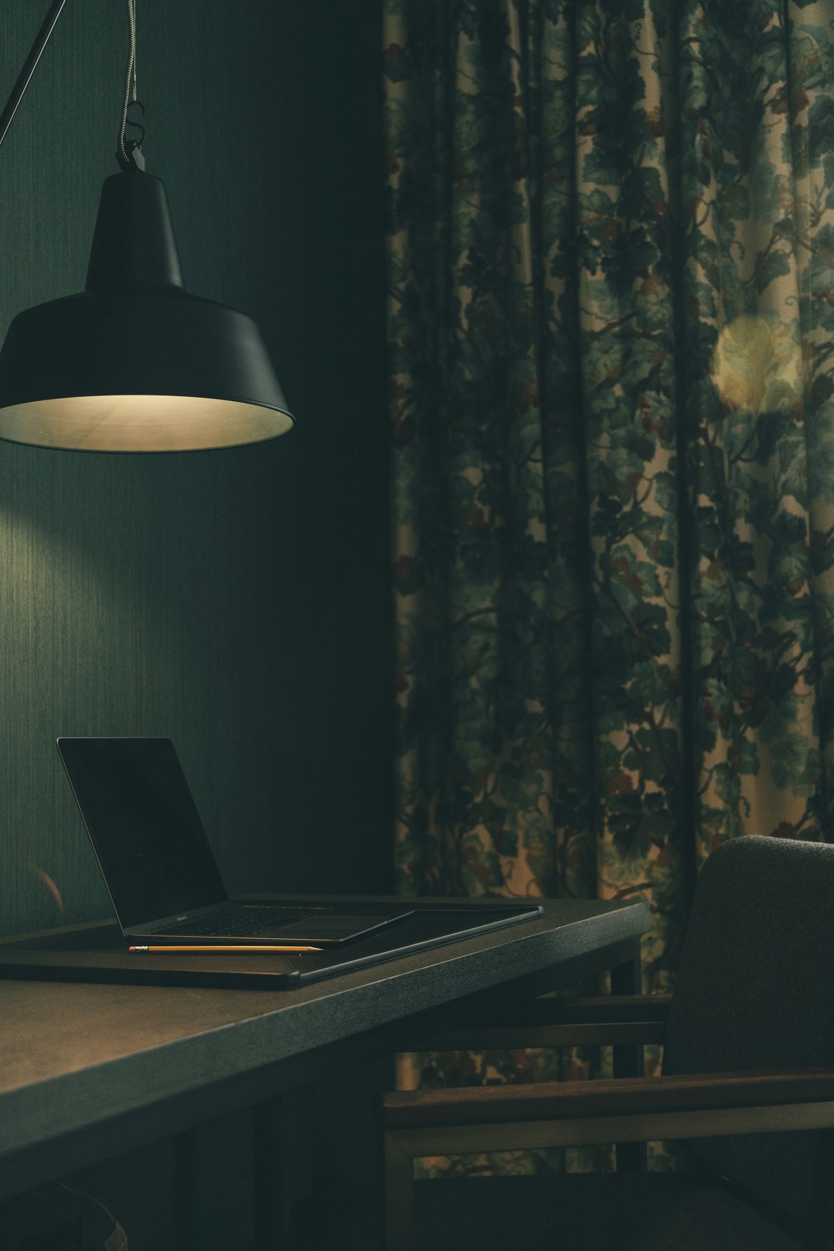 A pendant lamp over a laptop on a dark desk, late in the day